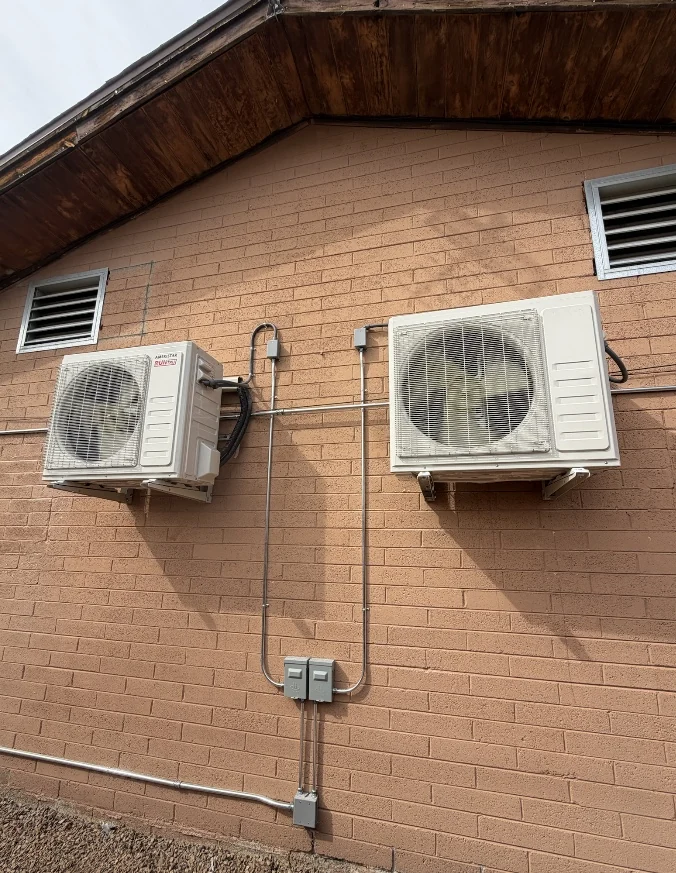 Two Mitsubishi mini-split condensers mounted on an exterior brick wall